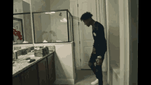 a man in a black shirt is standing in a bathroom looking at himself in the mirror