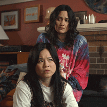 two women are sitting in front of a fireplace and one of them is wearing a tie dye shirt