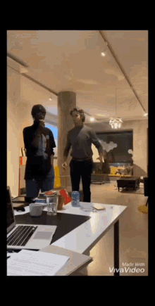 two men are standing in a room with a laptop on a desk