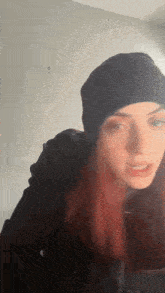 a woman with red hair is wearing a black beanie and making a funny face .