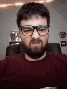 a man wearing glasses and a maroon shirt is making a funny face
