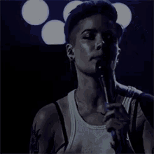 a man in a white tank top is singing into a microphone on a stage .