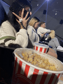 a striped bucket of popcorn sits on a table in front of a woman wearing a virtual reality headset