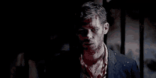 a man with blood on his face is standing in the dark in a dark room .