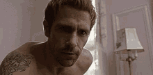 a shirtless man with a tattoo on his arm is standing in front of a lamp .