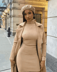 a woman wearing a beret and a tan dress is standing on a sidewalk
