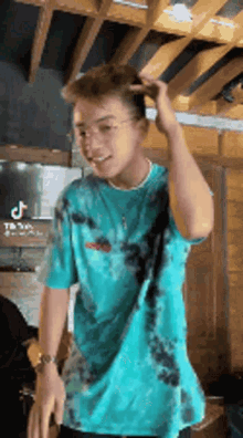 a young man in a blue tie dye t-shirt is standing in a room .
