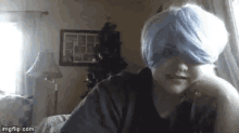 a young boy wearing a blue wig is sitting on a couch in a living room .