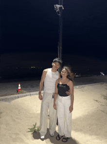 a man and a woman standing next to each other on the beach at night