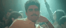 a man with a mustache is dancing in a crowd of people at a club .