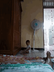 a baby sits in front of a fan in a room