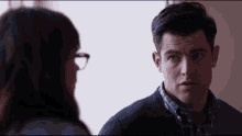 a man in a blue sweater talks to a woman with glasses
