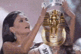 a woman is holding a crown over a statue of a pharaoh on her head .