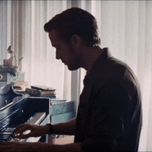 a man playing a piano in front of a window with books on it
