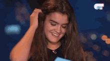 a woman with long hair is smiling and holding a piece of paper