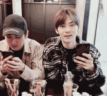 two young men are sitting at a table looking at their cell phones with the word cherry behind them