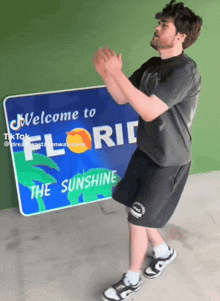 a man stands in front of a sign that says welcome to florida the sunshine