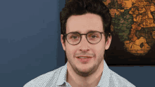 a man wearing glasses is smiling in front of a map of the world