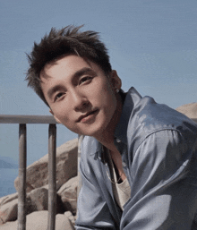 a young man in a blue shirt is leaning against a railing and looking at the camera