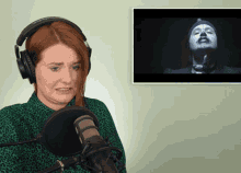 a woman wearing headphones stands in front of a microphone with a picture of a man in the background