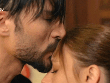 a man with a beard kisses a woman on the forehead with a tv logo in the background