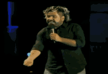 a man in a black shirt is holding a microphone in a dark room