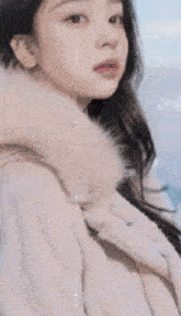 a woman wearing a white coat with a fur hood is standing on a beach .