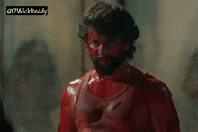 a man with a beard is covered in red paint and has a bullet hole in his chest .