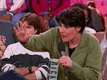 a woman in a green jacket is talking into a microphone with a sign that says rick on it