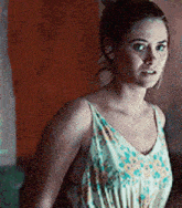 a woman in a white floral dress is standing in front of a wall .