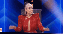 a woman in a red sequined dress is sitting at a table with her hands outstretched