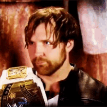 a man with a beard is holding a wrestling championship belt in his hand .