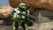 a man in a green helmet is holding a rifle in front of a rock