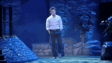 a man in a white shirt is standing on a stage in front of a stone wall