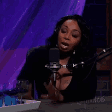 a woman wearing headphones is talking into a microphone while sitting at a table with a tray of wine glasses