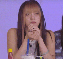a woman with long hair is sitting at a table with her hands folded and a drink in her hand .