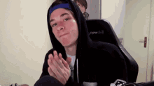 a young man wearing a hooded sweatshirt and a blue hat is clapping his hands .