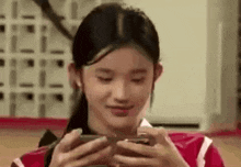 a young girl is holding a cell phone in her hands and smiling .
