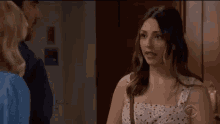 a woman in a white dress is standing in front of a door talking to a man and two women .