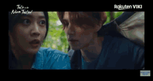 a man and a woman are standing next to each other in a forest and looking at each other .