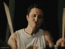 a man in a white tank top is playing drums in a dark room