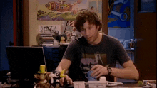 a man is sitting at a desk in front of a laptop with a poster on the wall behind him