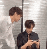 two men are standing next to each other in a room and one of them is looking at a cell phone .