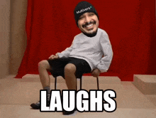 a man wearing a hat that says multiverse sits on a chair and says laughs