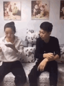 a man and a woman are sitting on a couch looking at their cell phones