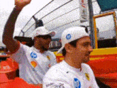 two men wearing white shirts and hats are sitting in a stadium .