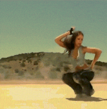 a woman is squatting down in the desert while holding a gun