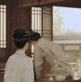 a man and a woman are sitting at a table in a room with a window .