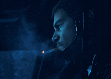 a man wearing a headset is smoking a cigarette in a dark room