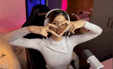 a woman wearing headphones making a heart with her hands